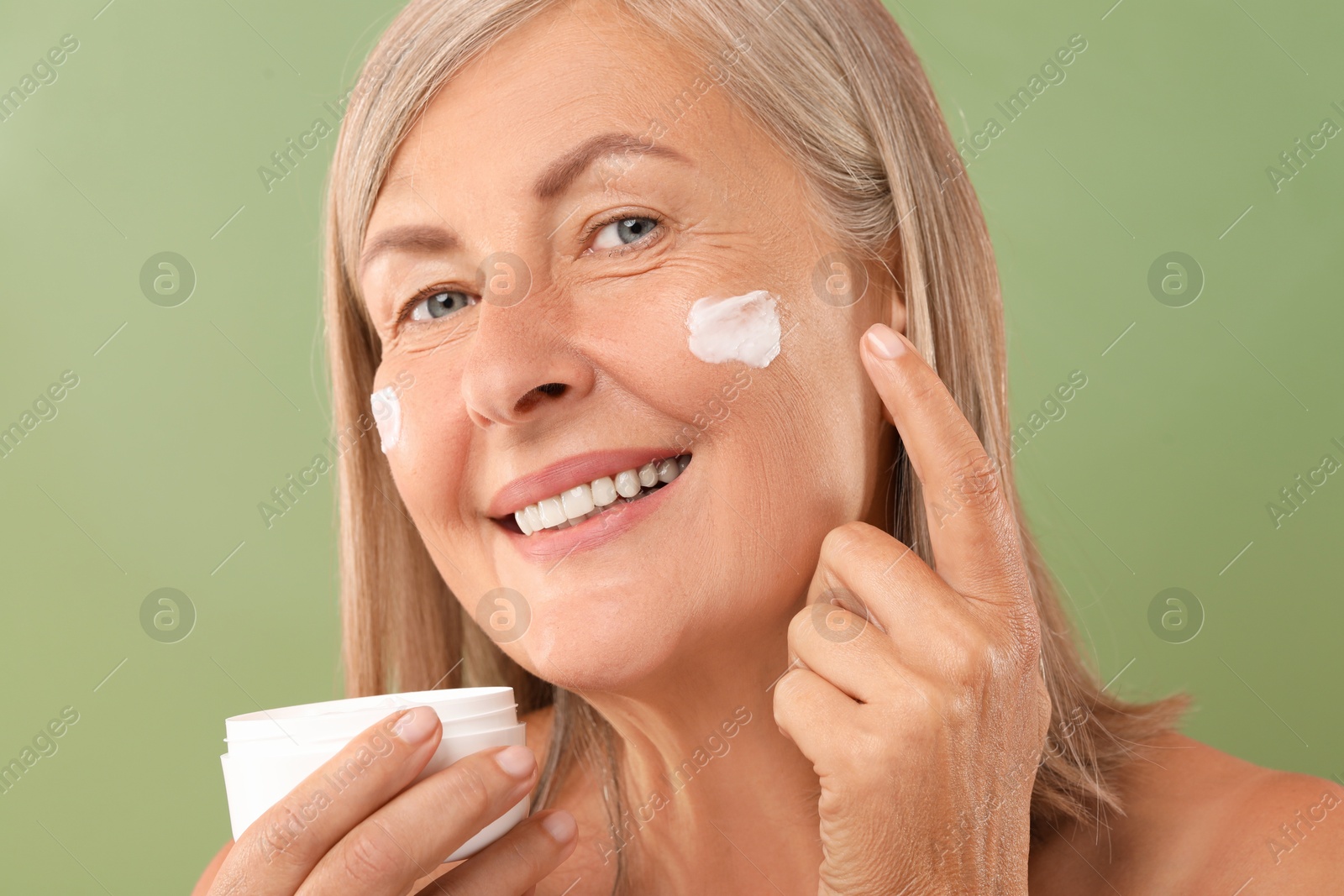 Photo of Senior woman applying face cream on green background, closeup