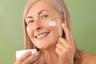 Photo of Senior woman applying face cream on green background, closeup