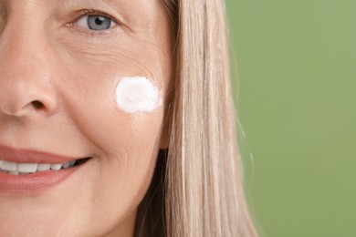 Photo of Senior woman with face cream on green background, closeup