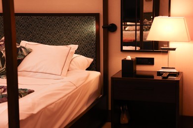 Comfortable bed and lamp on bedside table in stylish hotel room