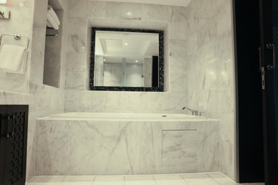 Stylish bathroom with marble bathtub and mirror in luxury hotel