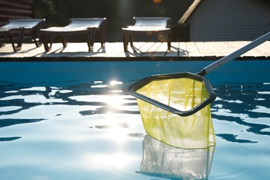 Cleaning swimming pool with skimmer net on sunny day