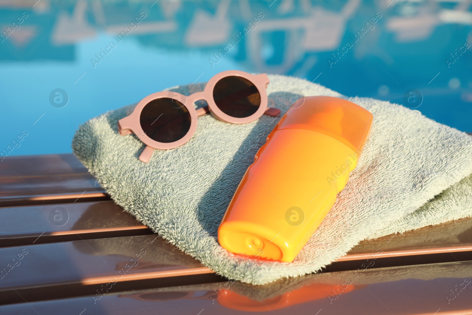 Photo of Stylish sunglasses, towel and sunscreen near outdoor swimming pool