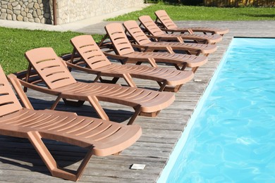 Photo of Empty sun loungers on wooden deck near outdoor swimming pool