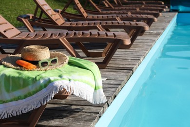 Photo of Beach accessories and sun loungers on wooden deck near outdoor swimming pool