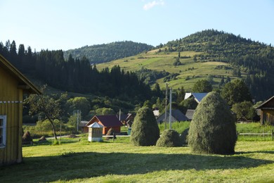 Beautiful view of haystacks, houses and forest in mountains under blue sky