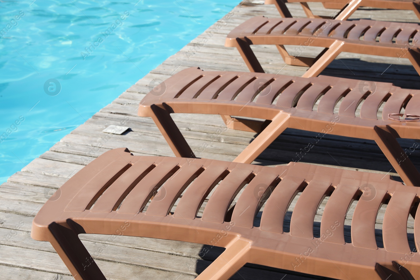 Photo of Empty sun loungers on wooden deck near outdoor swimming pool, closeup