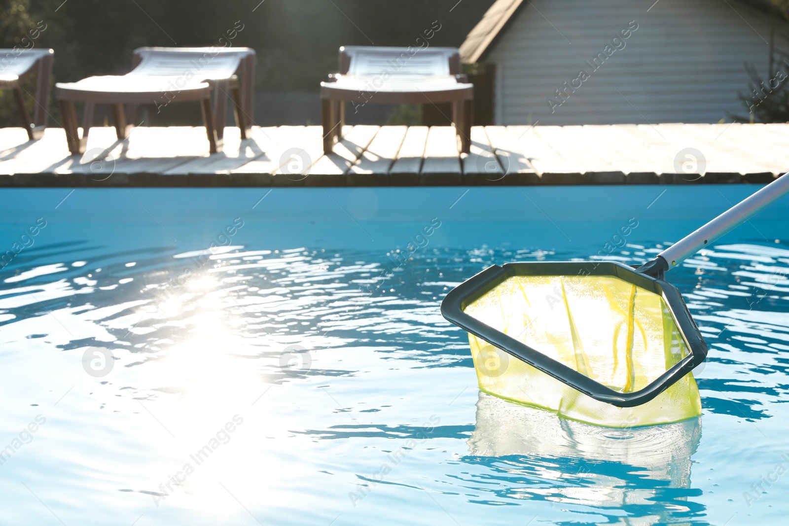 Photo of Cleaning swimming pool with skimmer net on sunny day