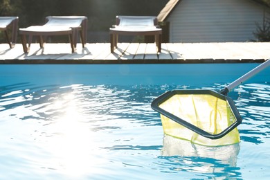 Photo of Cleaning swimming pool with skimmer net on sunny day