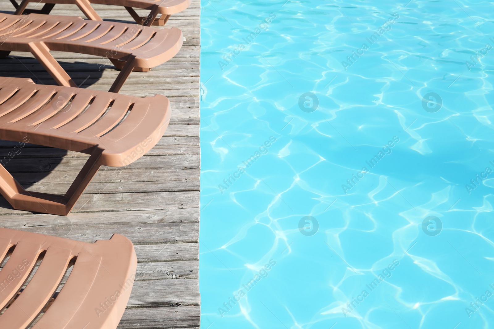 Photo of Empty sun loungers on wooden deck near outdoor swimming pool