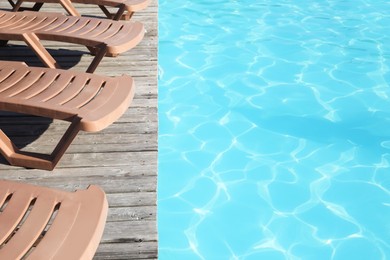 Photo of Empty sun loungers on wooden deck near outdoor swimming pool