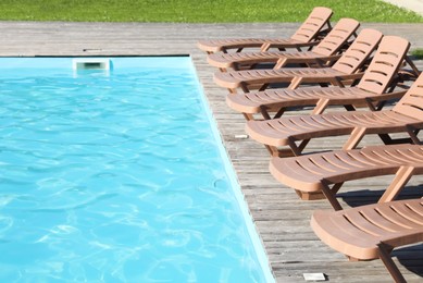 Photo of Empty sun loungers on wooden deck near outdoor swimming pool