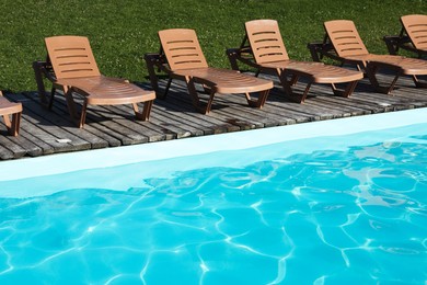 Photo of Empty sun loungers on wooden deck near outdoor swimming pool