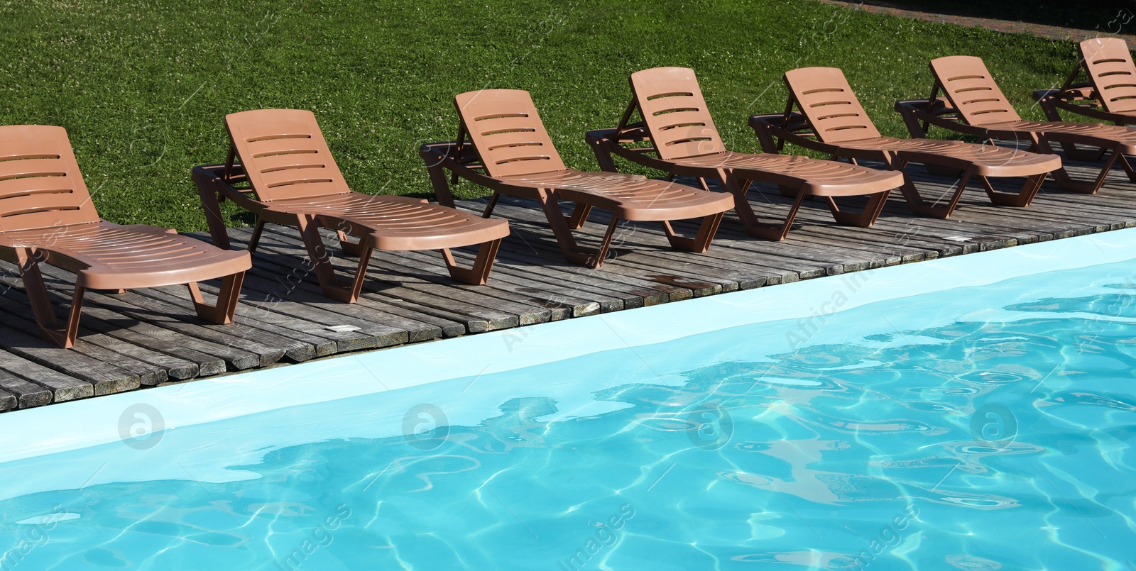 Photo of Empty sun loungers on wooden deck near outdoor swimming pool