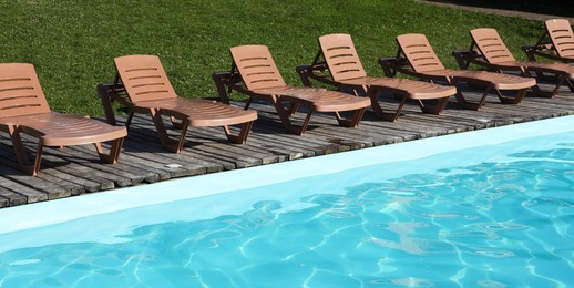 Photo of Empty sun loungers on wooden deck near outdoor swimming pool