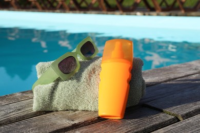 Photo of Stylish sunglasses, towel and sunscreen on wooden deck near outdoor swimming pool