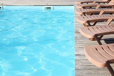 Photo of Empty sun loungers on wooden deck near outdoor swimming pool