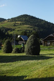 Photo of Beautiful view of haystacks, houses and forest in mountains under blue sky