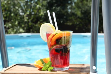 Photo of Tasty cocktail in glass near swimming pool outdoors