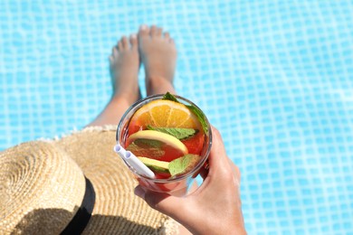 Photo of Woman holding tasty cocktail in glass near swimming pool outdoors, closeup