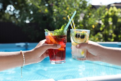 Photo of Women holding tasty cocktail in glass near swimming pool outdoors, closeup