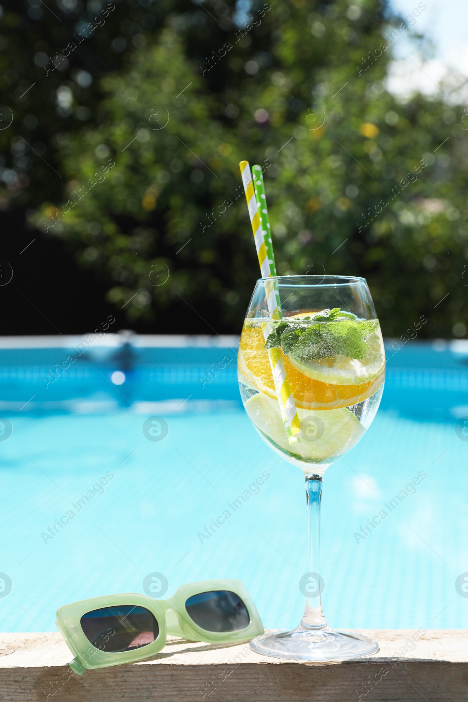 Photo of Tasty cocktail in glass and sunglasses near swimming pool outdoors