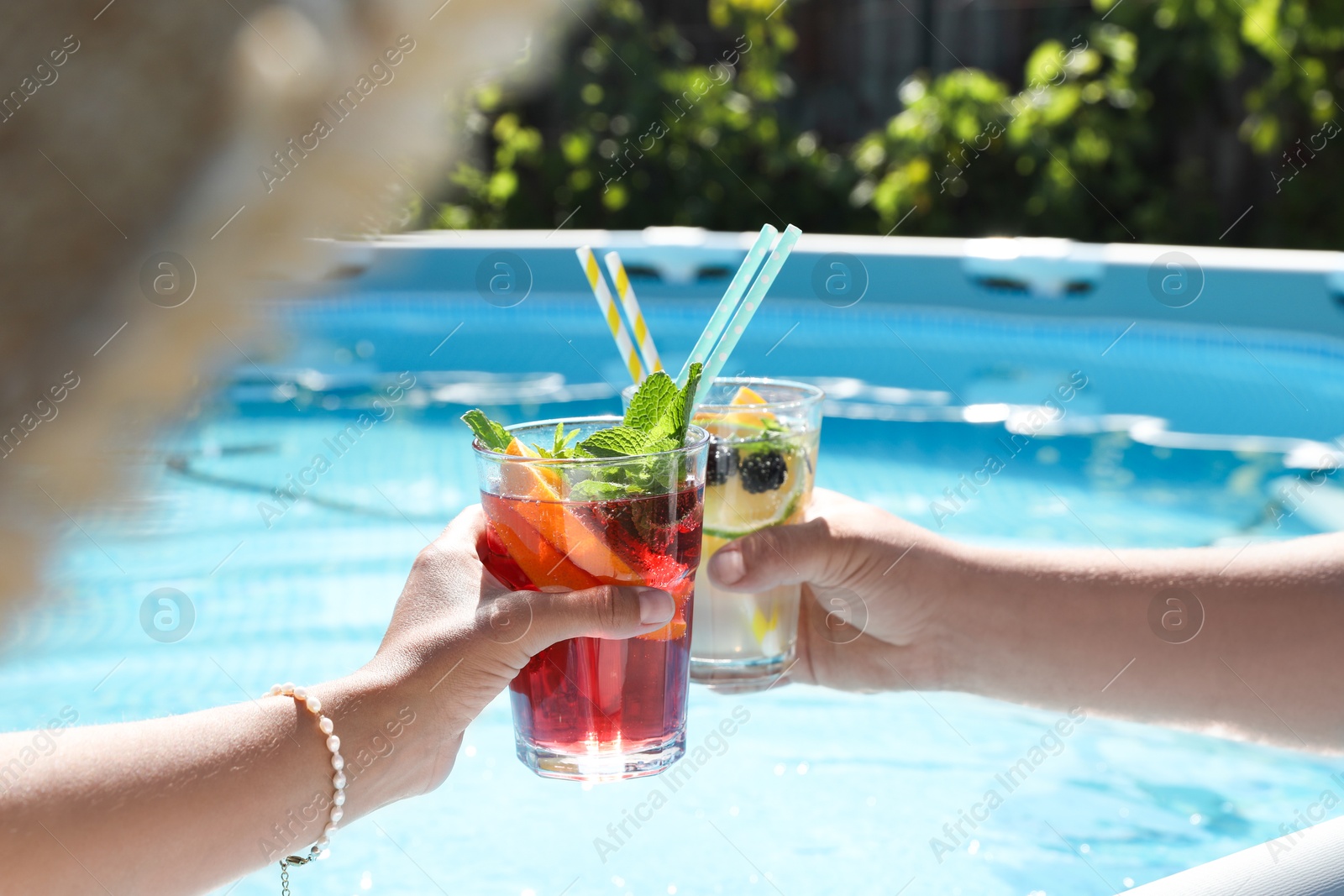 Photo of Women holding tasty cocktail in glass near swimming pool outdoors, closeup