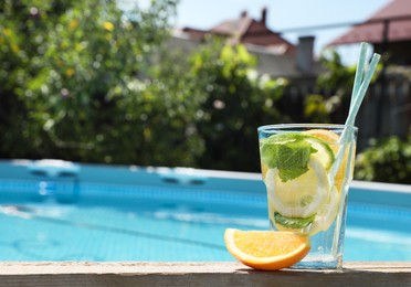 Photo of Tasty cocktail in glass near swimming pool outdoors, space for text