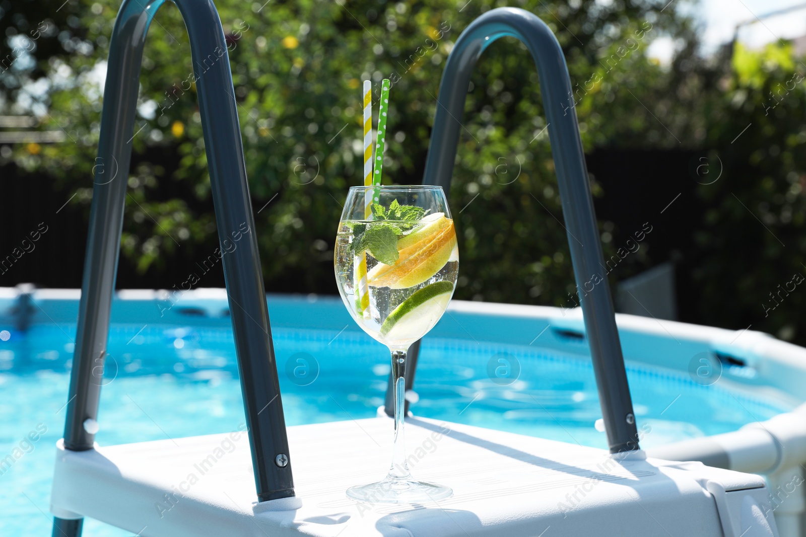 Photo of Tasty cocktail in glass near swimming pool outdoors