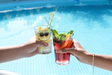 Photo of Women holding tasty cocktail in glass near swimming pool outdoors, closeup