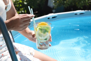 Woman holding tasty cocktail in glass near swimming pool outdoors, closeup