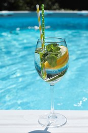 Photo of Tasty cocktail in glass near swimming pool outdoors