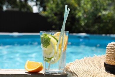 Photo of Tasty cocktail in glass and straw hat near swimming pool outdoors