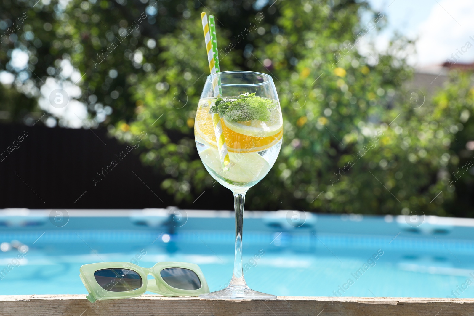 Photo of Tasty cocktail in glass and sunglasses near swimming pool outdoors