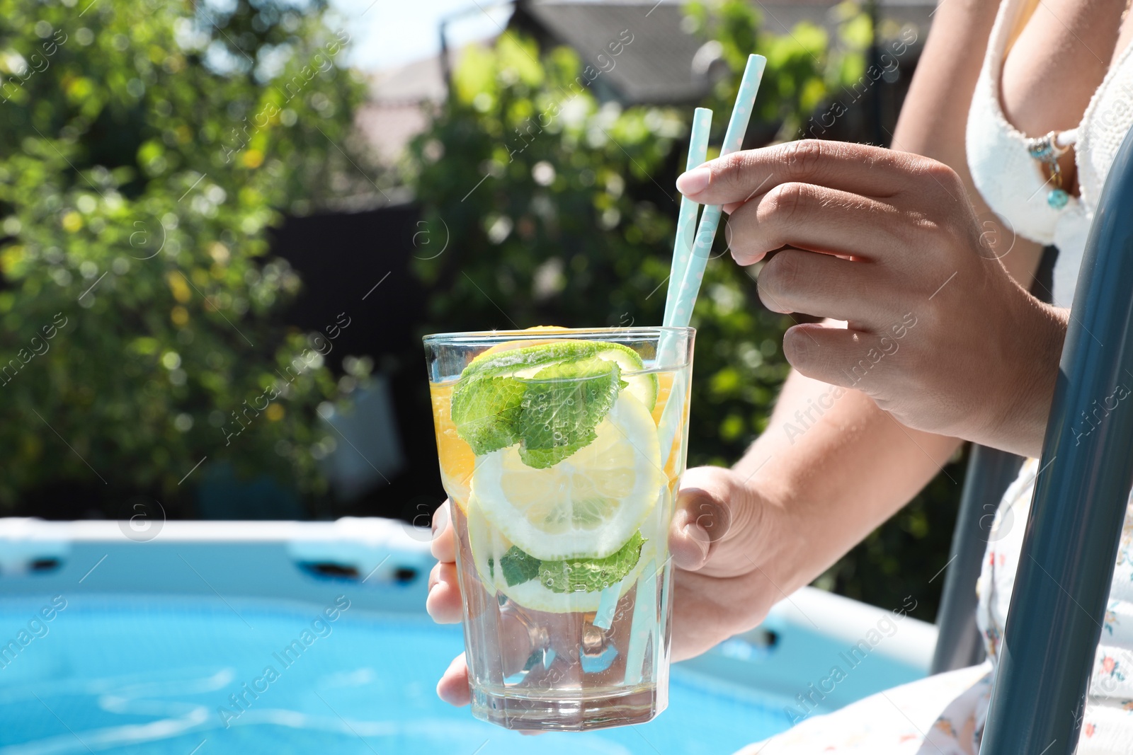 Photo of Woman holding tasty cocktail in glass near swimming pool outdoors, closeup