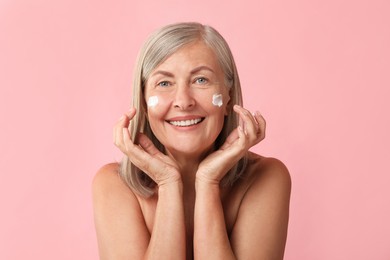 Senior woman with face cream on pink background