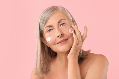 Photo of Senior woman applying face cream on pink background