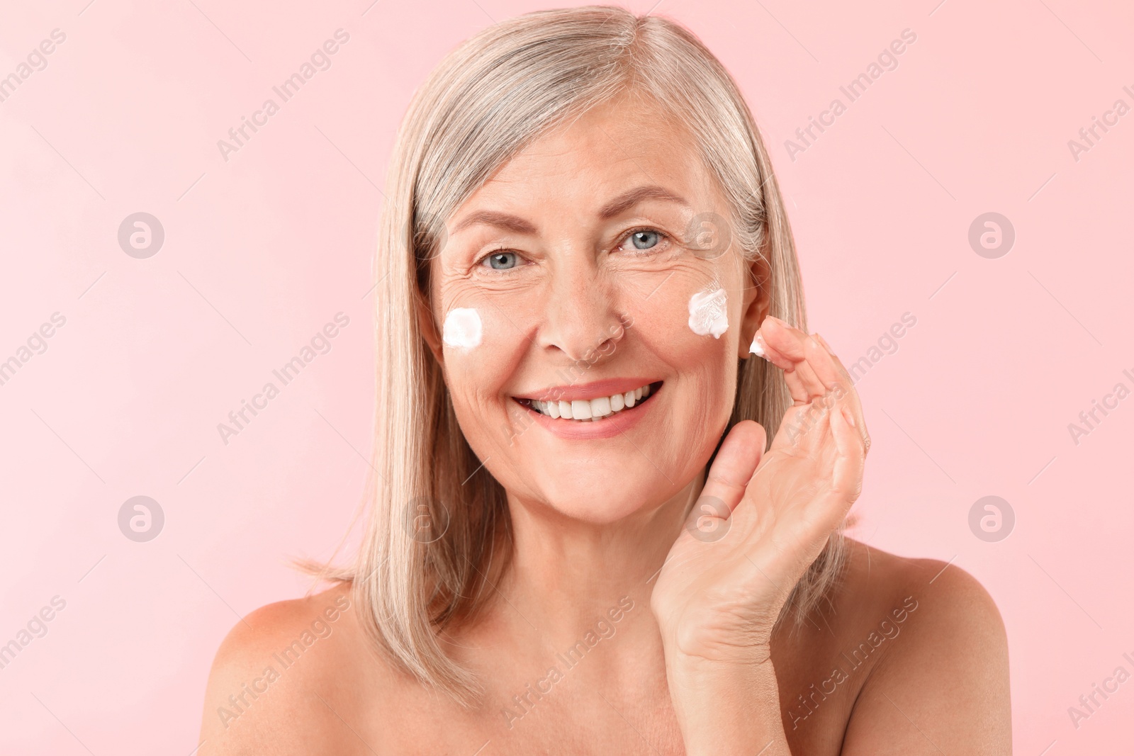 Photo of Senior woman applying face cream on pink background