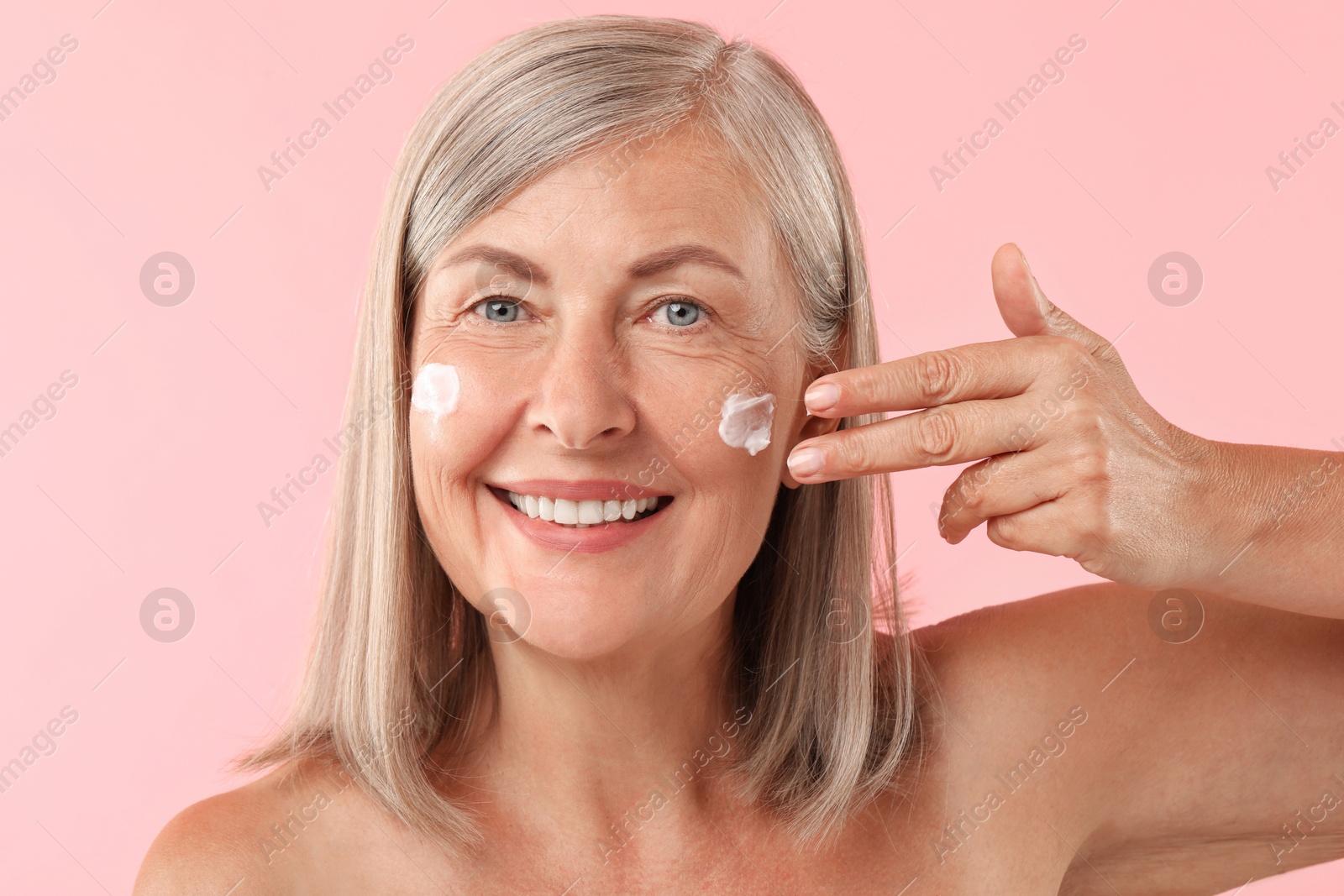 Photo of Senior woman applying face cream on pink background