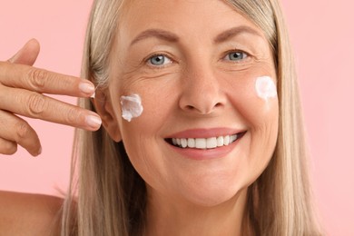 Photo of Senior woman applying face cream on pink background, closeup