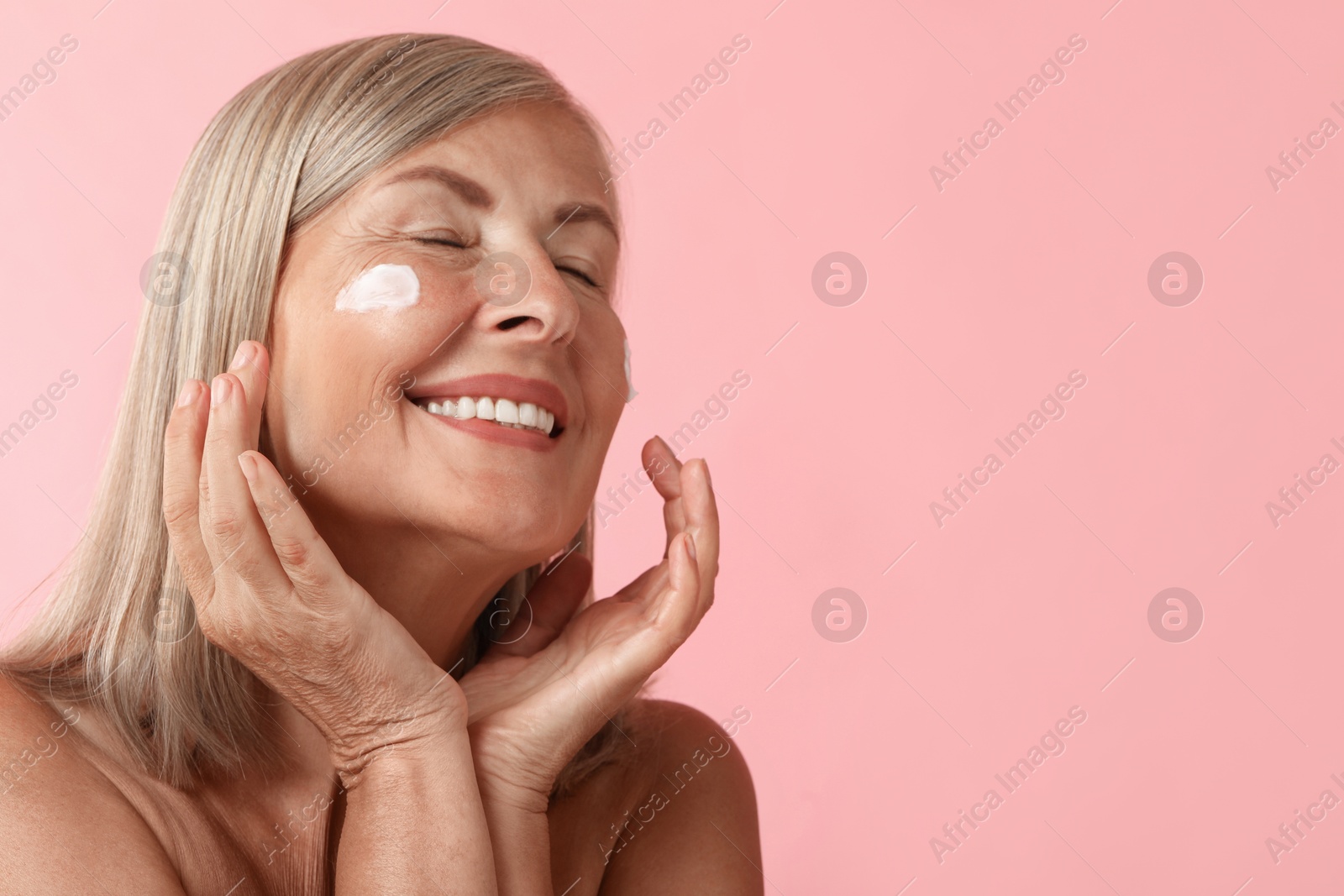 Photo of Senior woman with face cream on pink background. Space for text