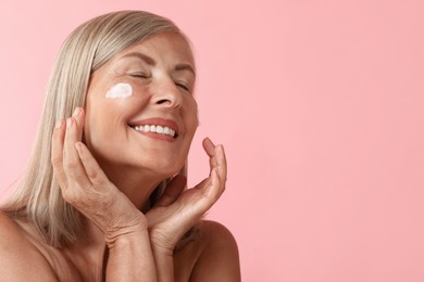 Senior woman with face cream on pink background. Space for text