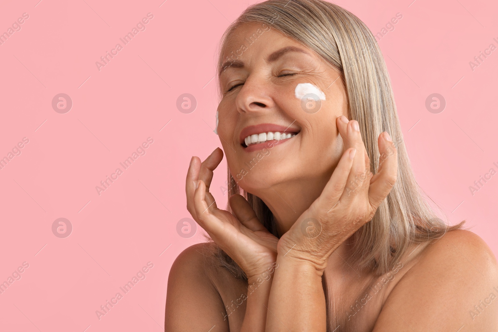 Photo of Senior woman with face cream on pink background