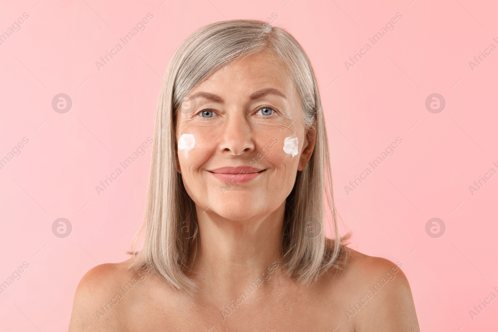 Photo of Senior woman with face cream on pink background