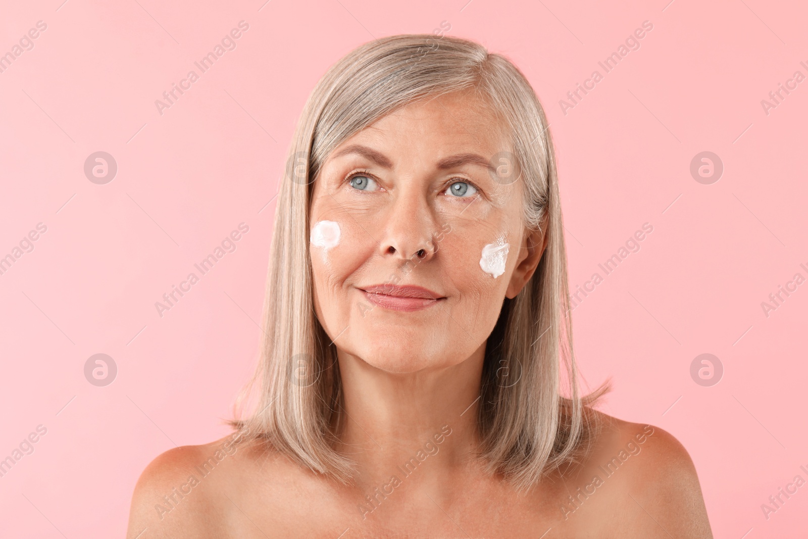 Photo of Senior woman with face cream on pink background