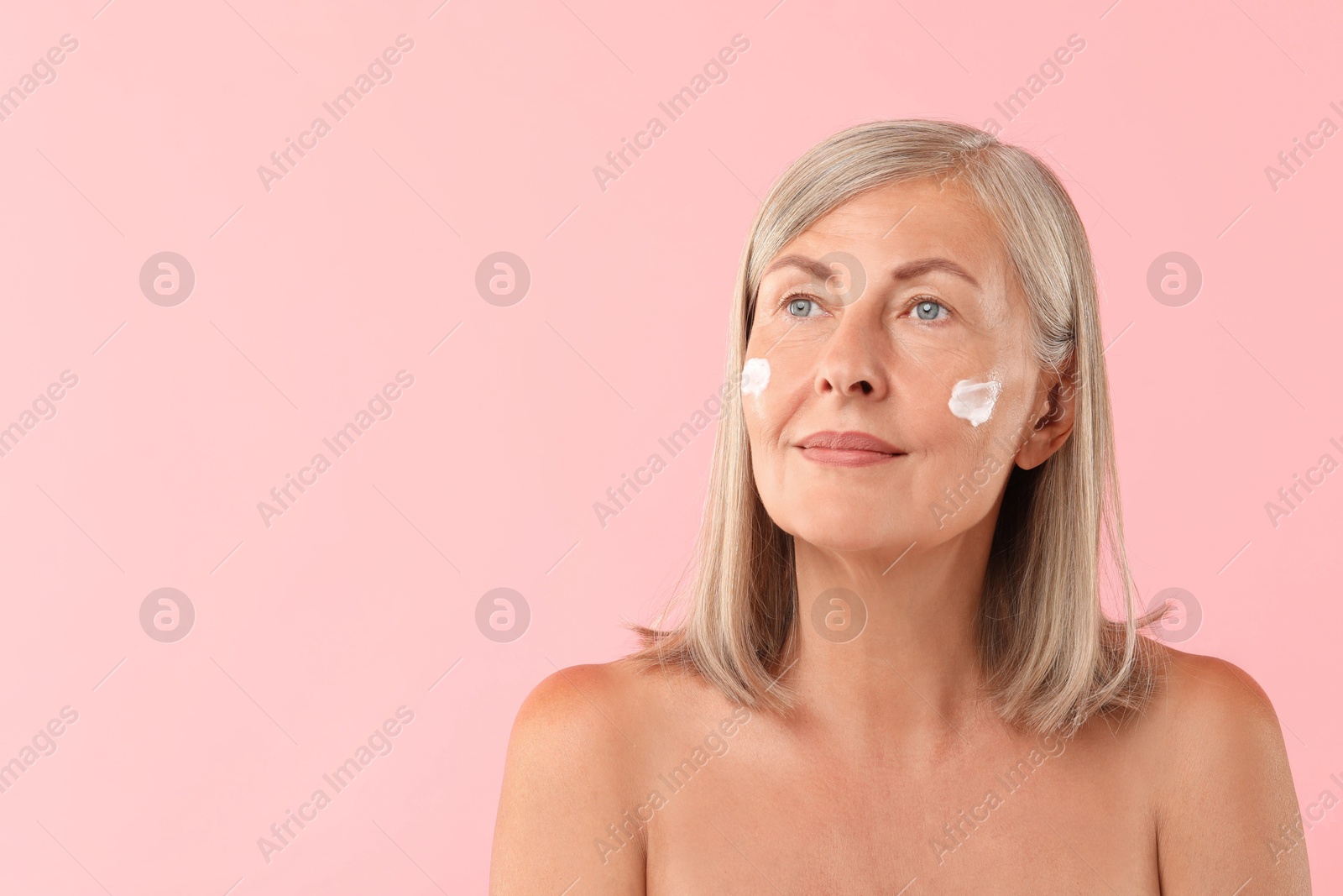 Photo of Senior woman with face cream on pink background. Space for text