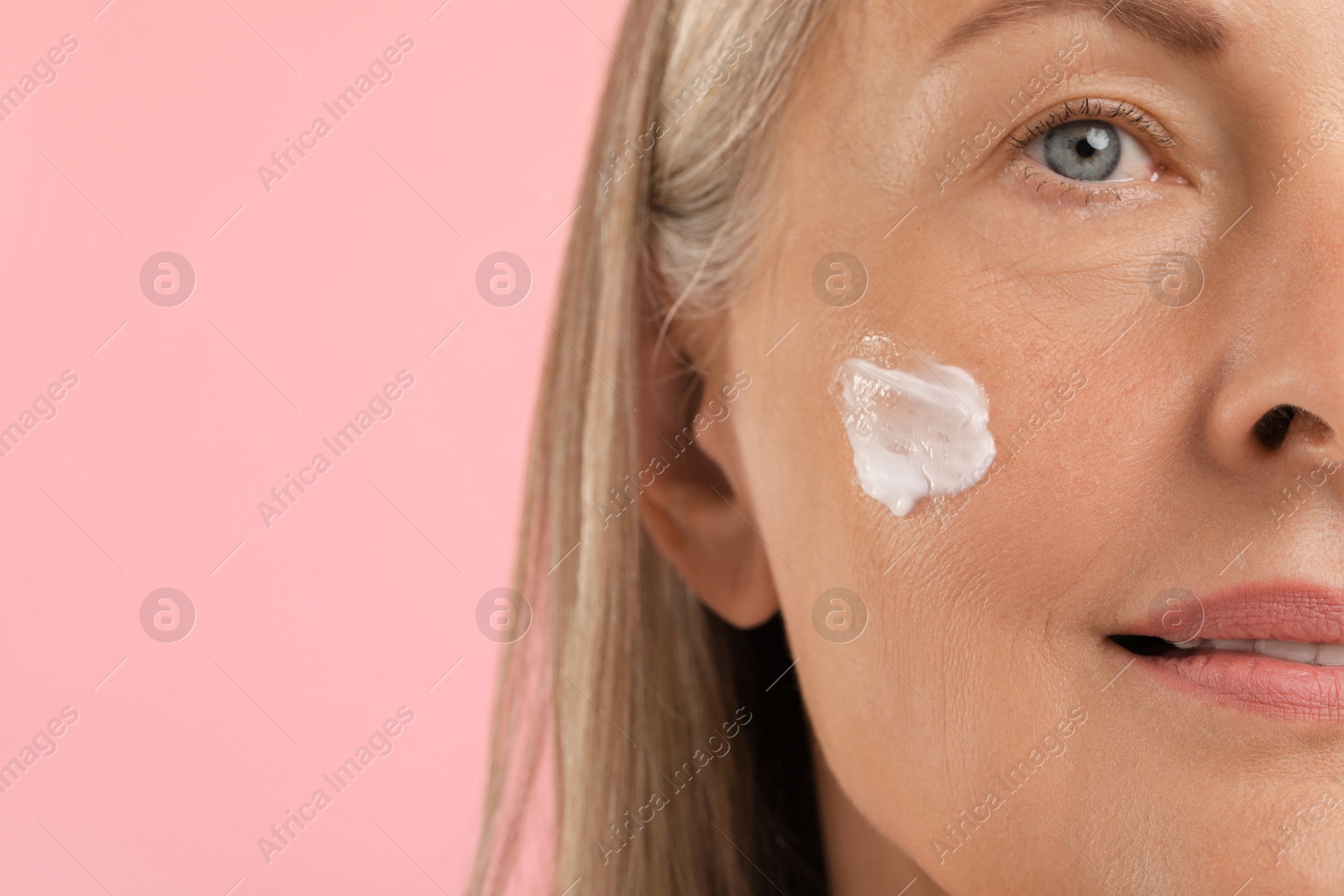 Photo of Senior woman with face cream on pink background, closeup. Space for text