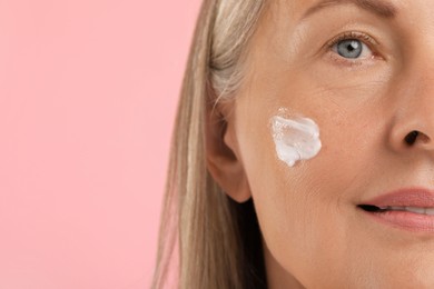 Senior woman with face cream on pink background, closeup. Space for text