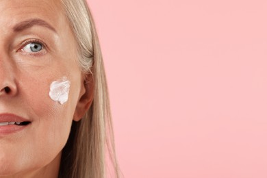 Photo of Senior woman with face cream on pink background, closeup. Space for text