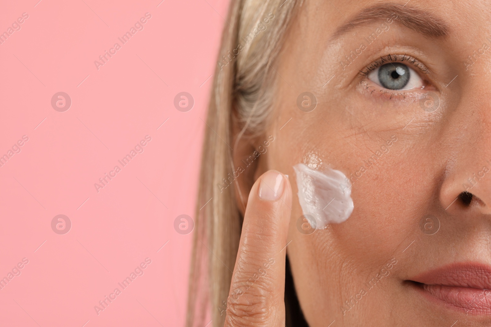 Photo of Senior woman applying face cream on pink background, closeup. Space for text